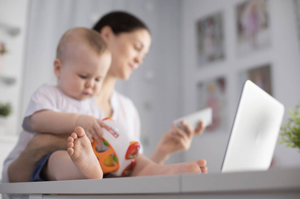 Jeune mère travaillant dans un décret à l'ordinateur avec un bébé fils dans ses bras
 - Photo, image