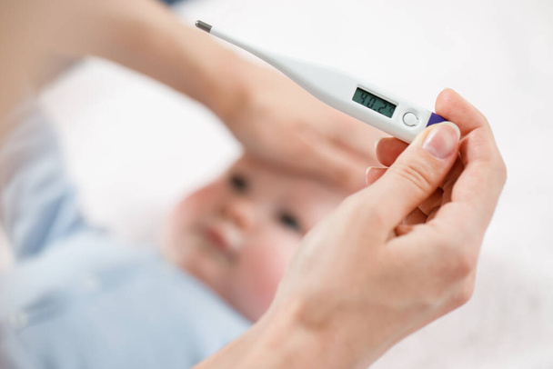 Close-up thermometer. Mother measuring temperature of her ill kid. Sick child with high fever laying in bed. Hand on forehead. - Photo, image