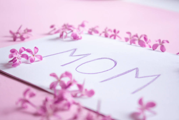 papier z napisem po angielsku "mama" i liliowe kwiaty na stole. koncepcja Dnia Matki, przesłanie i gratulacje. - Zdjęcie, obraz