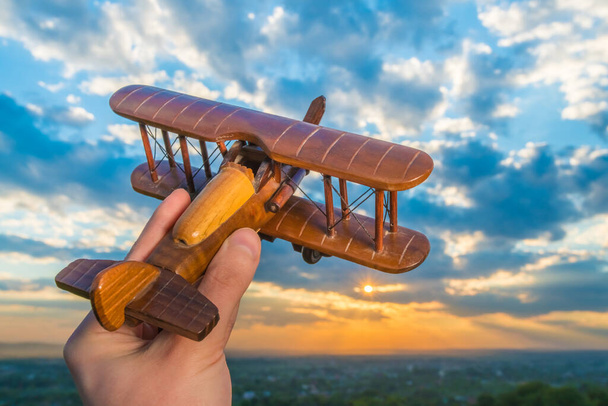 A mão segura o avião de madeira no fundo de um céu
 - Foto, Imagem