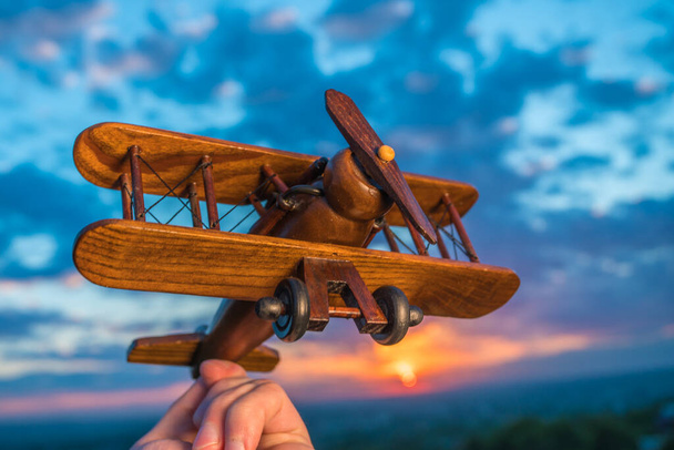 De hand met een speelgoedvliegtuigje tegen de achtergrond van een zonsondergang - Foto, afbeelding