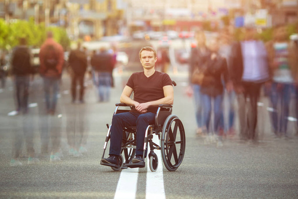 Niepełnosprawny siedzi na wózku inwalidzkim przy drodze z ludźmi. - Zdjęcie, obraz