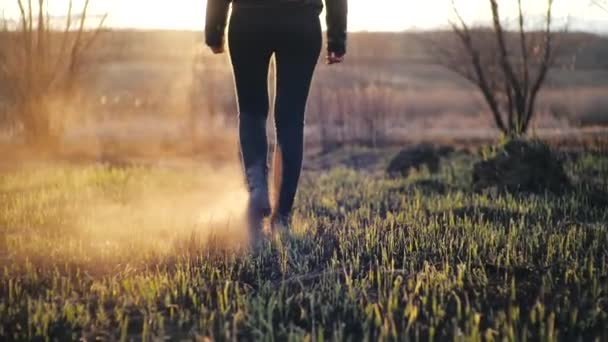 Yanmış kül çimlerinin önünde yürüyen bir kızın arka planda, siyah tozluklarla ve şık deri çizmelerle yanan bir sonbahar tarlasına doğru yürümesi. Duman tabanın altından geliyor.. - Video, Çekim