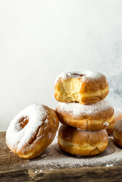 Lush sweet homemade donuts sprinkled with powdered sugar on a wooden background - Photo, Image
