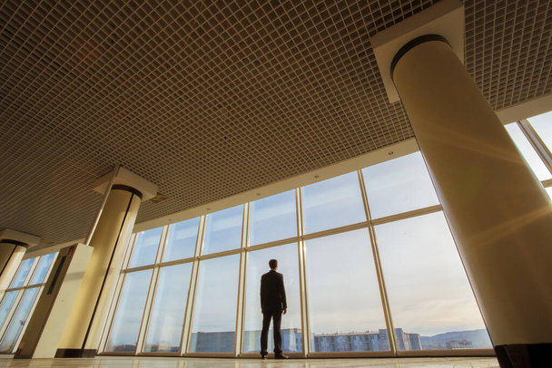 Мужчина стоит у панорамного окна на фоне заката
 - Фото, изображение