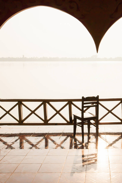 Ein ruhiger alter Pavillon am Mekong in der Abenddämmerung, leerer alter Pavillon mit Blick auf Holzstühle von innen nach außen, ländliche Szenerie in Champasak, Südlaos. Öffentlicher Raum. - Foto, Bild