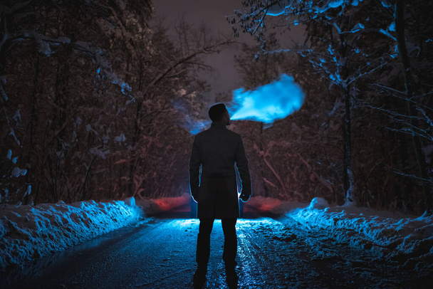 O homem fuma na estrada nevada da floresta. noite noite tempo
 - Foto, Imagem