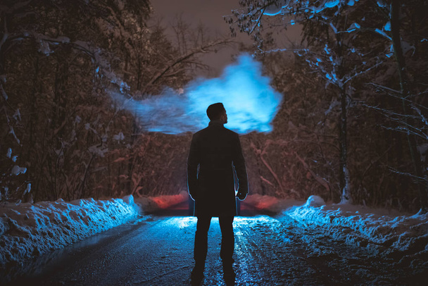 The man smoke on the snowy road in the forest. evening night time - Photo, Image