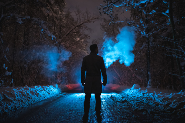 De man rookt op de besneeuwde weg in het donkere bos. avond nacht tijd - Foto, afbeelding