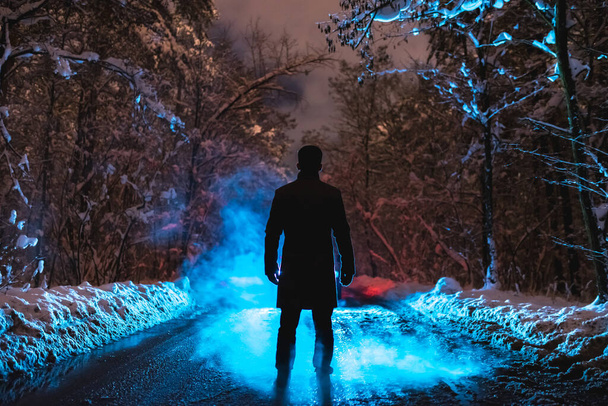 L'homme se tient près de la fumée bleue dans la forêt d'hiver. soir heure de nuit
 - Photo, image