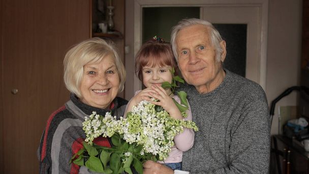 Kleindochter omarmt senior lachende grootvader met grootmoeder thuis - Foto, afbeelding