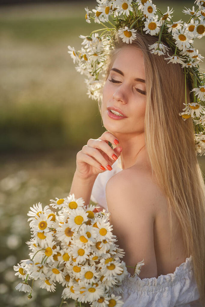 portrait of a beautiful blonde woman on meadow looking to the camera and enjoying nature spring evening outdoors. Caucasian woman relaxation in the park with daisy outside with copy space, cover - Fotó, kép