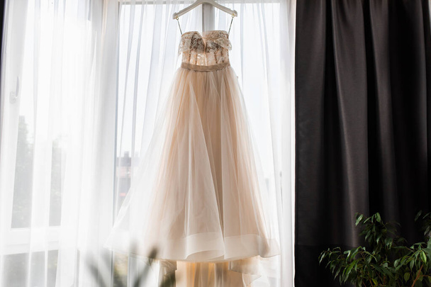 Гарна біла весільна сукня. Весільна сукня висить на вікні. Підсвічування
. - Фото, зображення