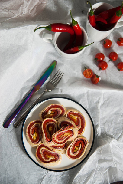 Wrapped Salami and Red Pepper Pickles with Tortilla Bread on a Wooden Cutting Board. White Plates and Paper Background - Photo, Image