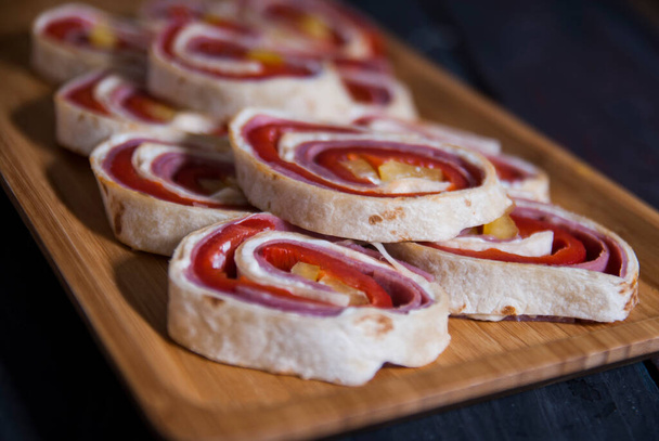 Csomagolt szalámi és vörös paprika uborka tortilla kenyérrel egy fa vágódeszkán. Fehér táblák és papír háttér - Fotó, kép