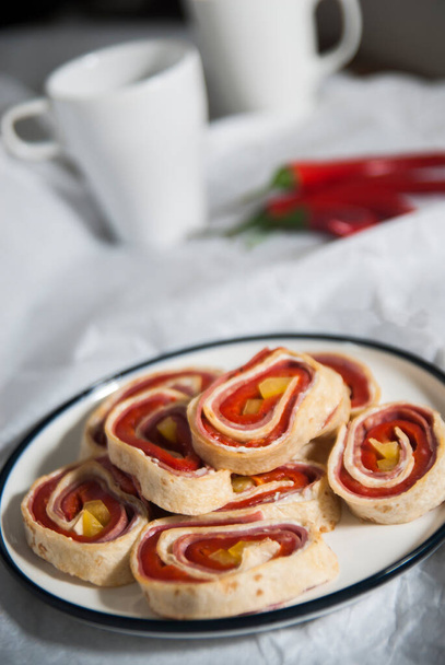 Τυλιγμένο σαλάμι και κόκκινη πιπεριά τουρσί με ψωμί τορτίγια σε μια ξύλινη επιφάνεια κοπής. Λευκά πιάτα και φόντο χαρτί - Φωτογραφία, εικόνα
