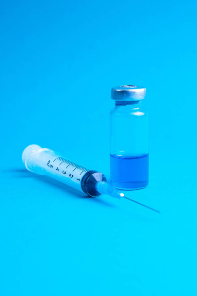 Glass vials and a medical syringe with a coronavirus vaccine on a blue background. - Foto, immagini