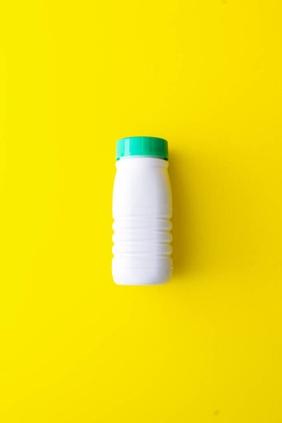 Botella de plástico blanco con una tapa verde sobre un fondo amarillo situado en el centro. Reciclaje de plástico en el contenedor amarillo
 - Foto, Imagen