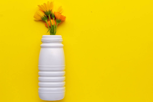 Botella de plástico blanco reutilizada con flores sobre un fondo amarillo situado a la izquierda. Reciclaje de plástico a contenedor amarillo
 - Foto, imagen
