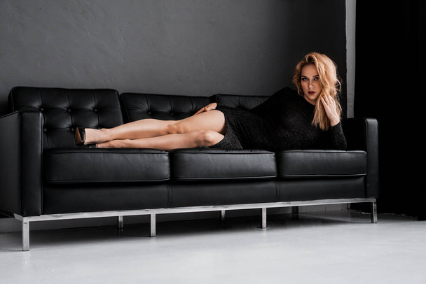 Beautiful girl in black dress lays on the couch - Zdjęcie, obraz