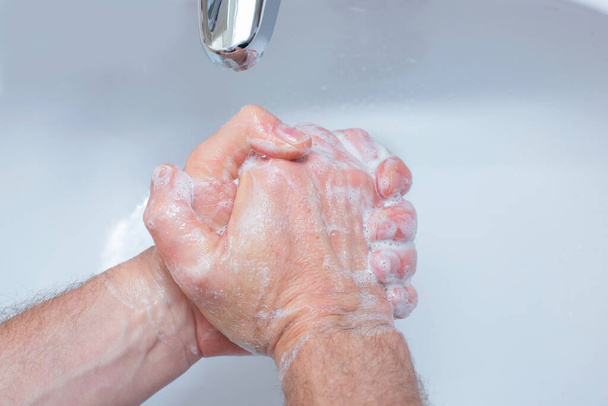 Um homem lava as mãos com sabão na casa de banho. A mão do homem de perto. Desinfecção das mãos e tratamento para o coronavírus. Regras de quarentena. Higiene pessoal
 - Foto, Imagem