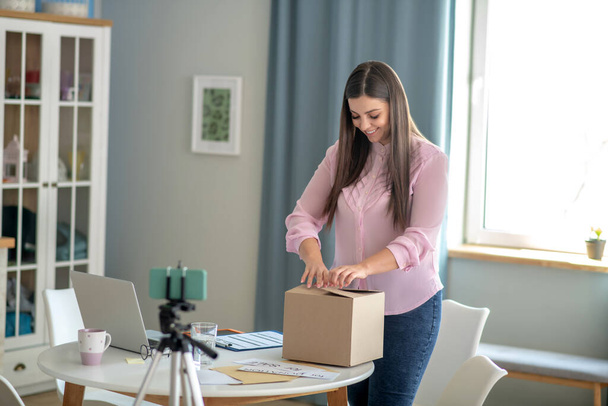 Dark-haired young woman in a pink blouse packing the box - 写真・画像