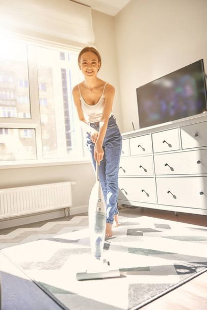 Cute young woman vacuuming floor in flat - Zdjęcie, obraz