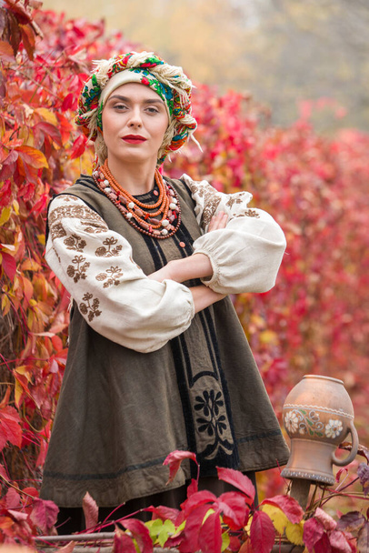 Piękna dziewczyna w sukience narodowej. Starożytnym glinianym garnkiem. Starożytna odzież z końca XIX wieku. Piękna sukienka i spódnica na kobiecie. Piękna jesień i liście. Odzież późnych 19-tych lat - Zdjęcie, obraz