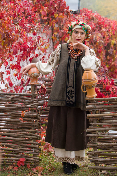 Beautiful girl in national dress. With an ancient clay pot. Antique clothing of the late 19th century. Beautiful dress and skirt on a woman. Beautiful autumn and leaves. Clothing of the late 19th - Photo, Image