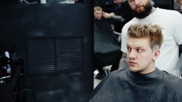 魅力的な男性は理容室の店で現代的な散髪を得ています。青いスプレーで顧客に髪を染めるバーバー. - 映像、動画