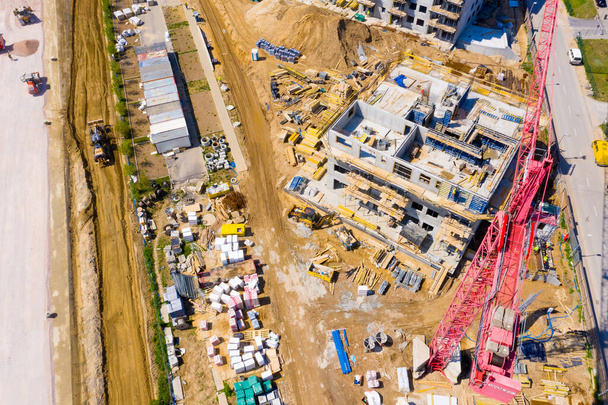 Aerial view of tower lifting crane and concrete frame of tall apartment residential building under construction in a city. Urban development and real estate growth concept. - Photo, Image