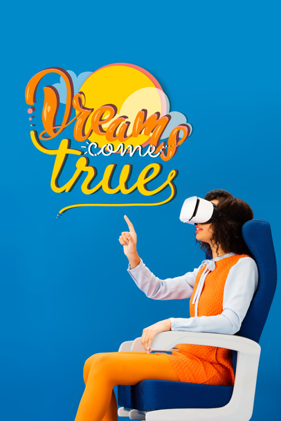 side view of african american with vr headset pointing with finger at dreams come true illustration on blue background - Photo, Image