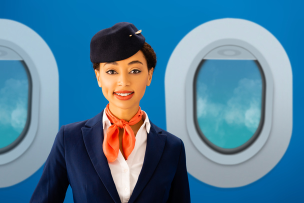 sorridente assistente di volo afroamericano che guarda la macchina fotografica con oblò su sfondo blu
 - Foto, immagini