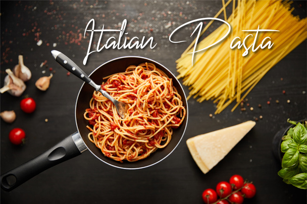 selective focus of tasty bolognese pasta in frying pan near ingredients on black wooden background, italian pasta illustration - Φωτογραφία, εικόνα