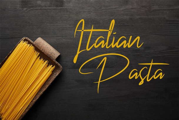 top view of raw spaghetti on black wooden background, italian pasta illustration - Foto, afbeelding