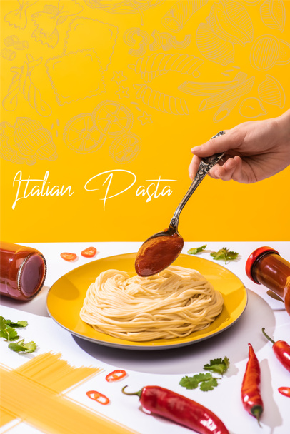Cropped view of woman adding ketchup to spaghetti on white surface isolated on yellow, Italian pasta illustration - Photo, Image