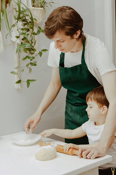 Boldog család a konyhában. Apa és fia elkészíti a tésztát, sütit süt. Alkalmi életmód otthon belső, szép gyermek, nyaralás koncepció, sodrófa, coockie vágó és tészta.  - Fotó, kép
