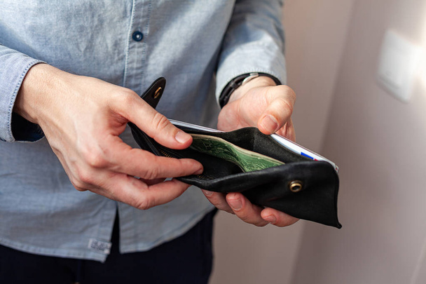Мужчина в джинсовой рубашке держит бумажник. Мужские руки и вынуть или положить $2 законопроект в бумажник. Концепция бедности и банкротства
 - Фото, изображение