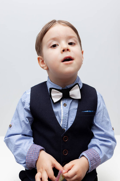A boy in a shirt, vest and trousers is eating a delicious candy. White background. The child is smart. Hair parted in the middle - Foto, imagen