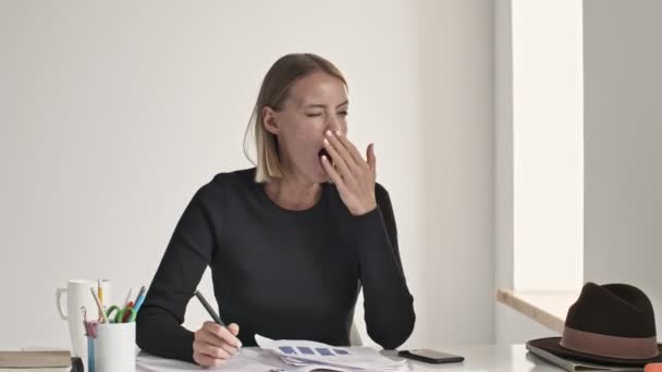 An attractive young blonde businesswoman is yawning while finishing her working day and do away from a white office - Felvétel, videó