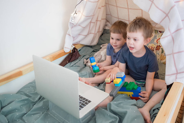 Niños pequeños sentados en la cama con portátil. Viendo dibujos animados, video chat, educación a distancia. bloqueo, cuarentena. Familia de estilo de vida
 - Foto, imagen