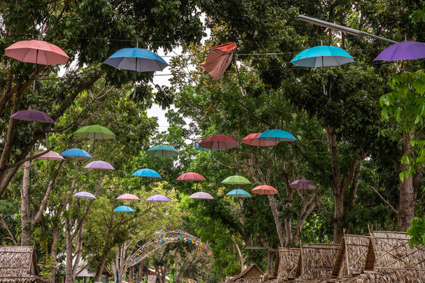 Paraguas de colores brillantes cuelgan en el aire visto desde abajo bajo un cielo azul dentro del festival tradicional de los aldeanos. paraguas colgando como decoración
. - Foto, Imagen
