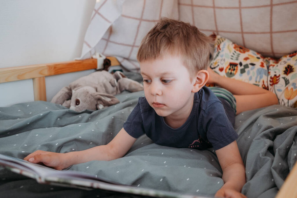 preschooler boy reading book laying in his bed. spending time at home. Lifestyle family concept - Fotó, kép