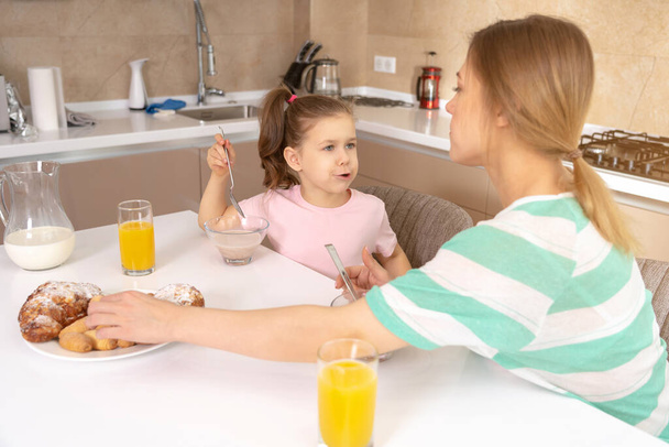 Mother having breakfast with her daughter at a table in kitchen, happy single mother concept - Photo, Image