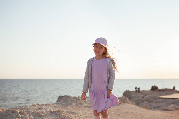 Happy pretty girl walks along the sea coast against the background of the sea, from behind a beautiful landscape - Fotografie, Obrázek