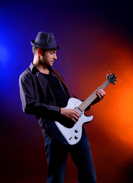 Young musician playing guitar on dark color background - Foto, imagen