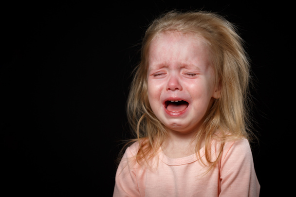 Een klein meisje huilt hysterisch in een donkere kamer. Ze was zwaar gewond. - Foto, afbeelding