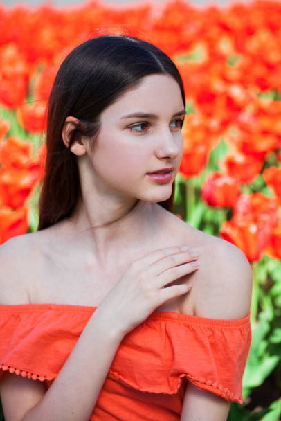 Portrait of a young beautiful girl posing on a background of red tulips - Foto, imagen