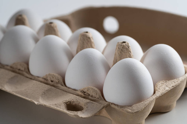 Nahaufnahme eines mit Heu und frischen und ausgewählten weißen Hühnereiern gefüllten Eierbechers. Seitenansicht. Porträtorientierung. Vorstellung des Konzepts der gesunden Ernährung oder Abbildung für Ihr Produkt - Foto, Bild