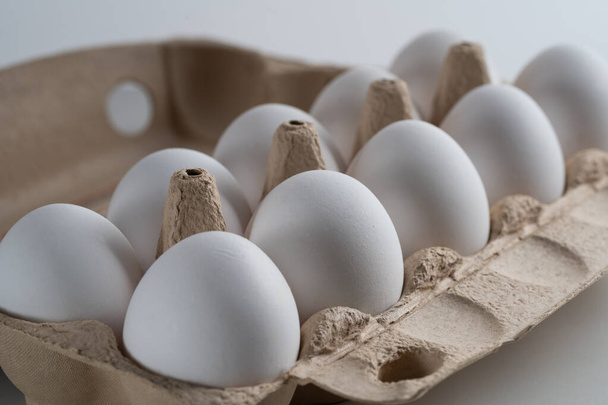 Primer plano de una bandeja de huevos llena de heno y huevos de pollo blancos frescos y seleccionados. Vista lateral. Orientación vertical. Represente el concepto de nutrición saludable o ilustración para su producto
 - Foto, imagen